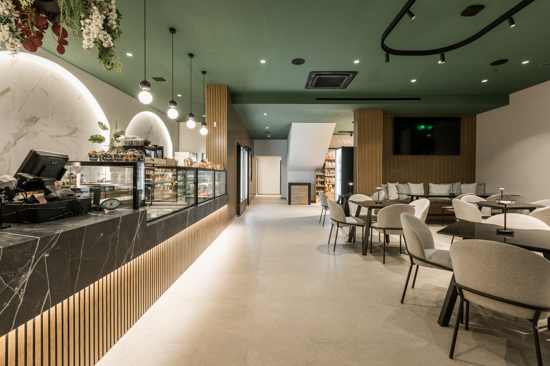 Εσωτερικός χώρος μοντέρνου καφέ με γκρι καθίσματα, ξύλινους τοίχους και πράσινη οροφή.