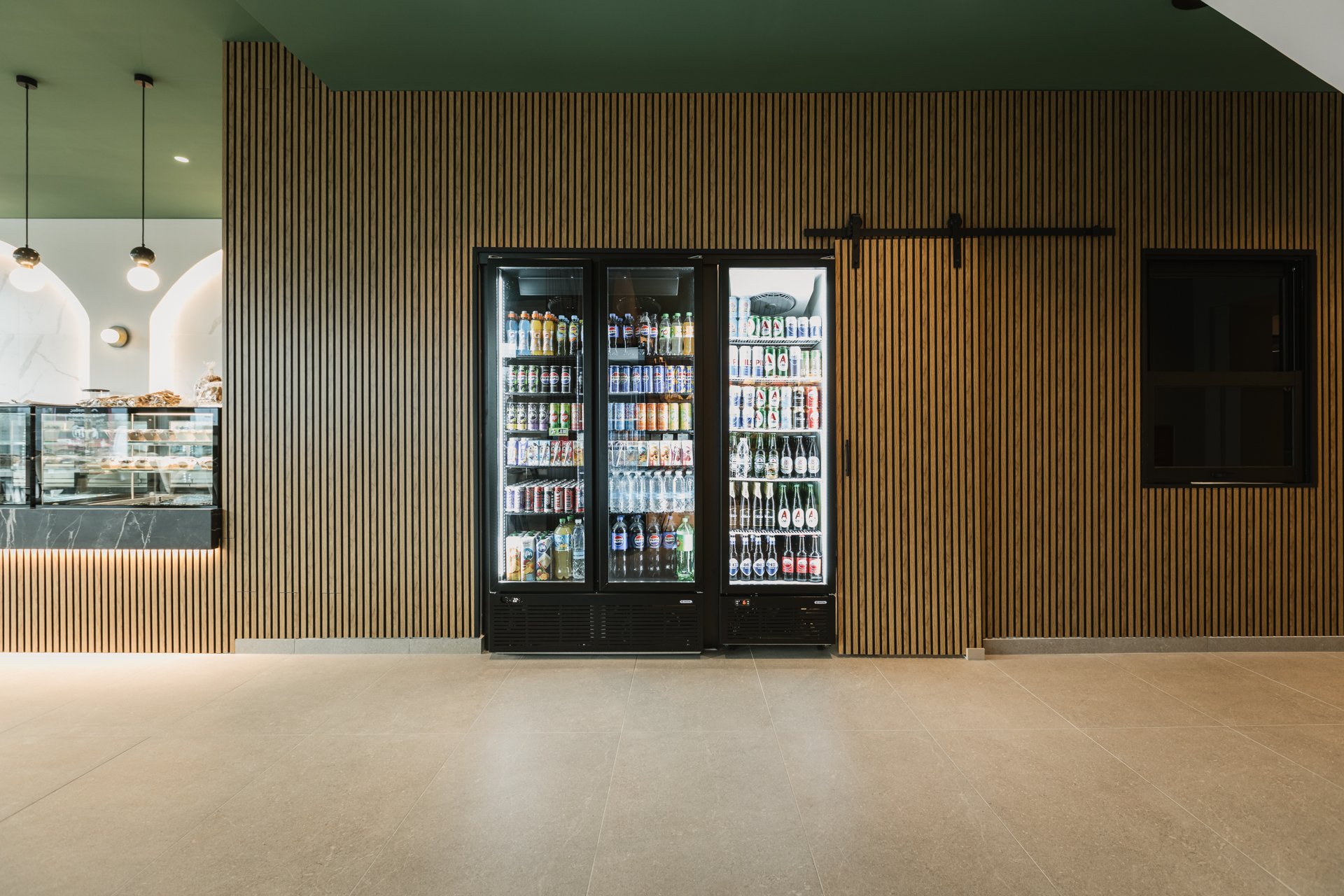 Εσωτερικός χώρος μοντέρνου καφέ με γκρι καθίσματα, ξύλινους τοίχους και πράσινη οροφή.