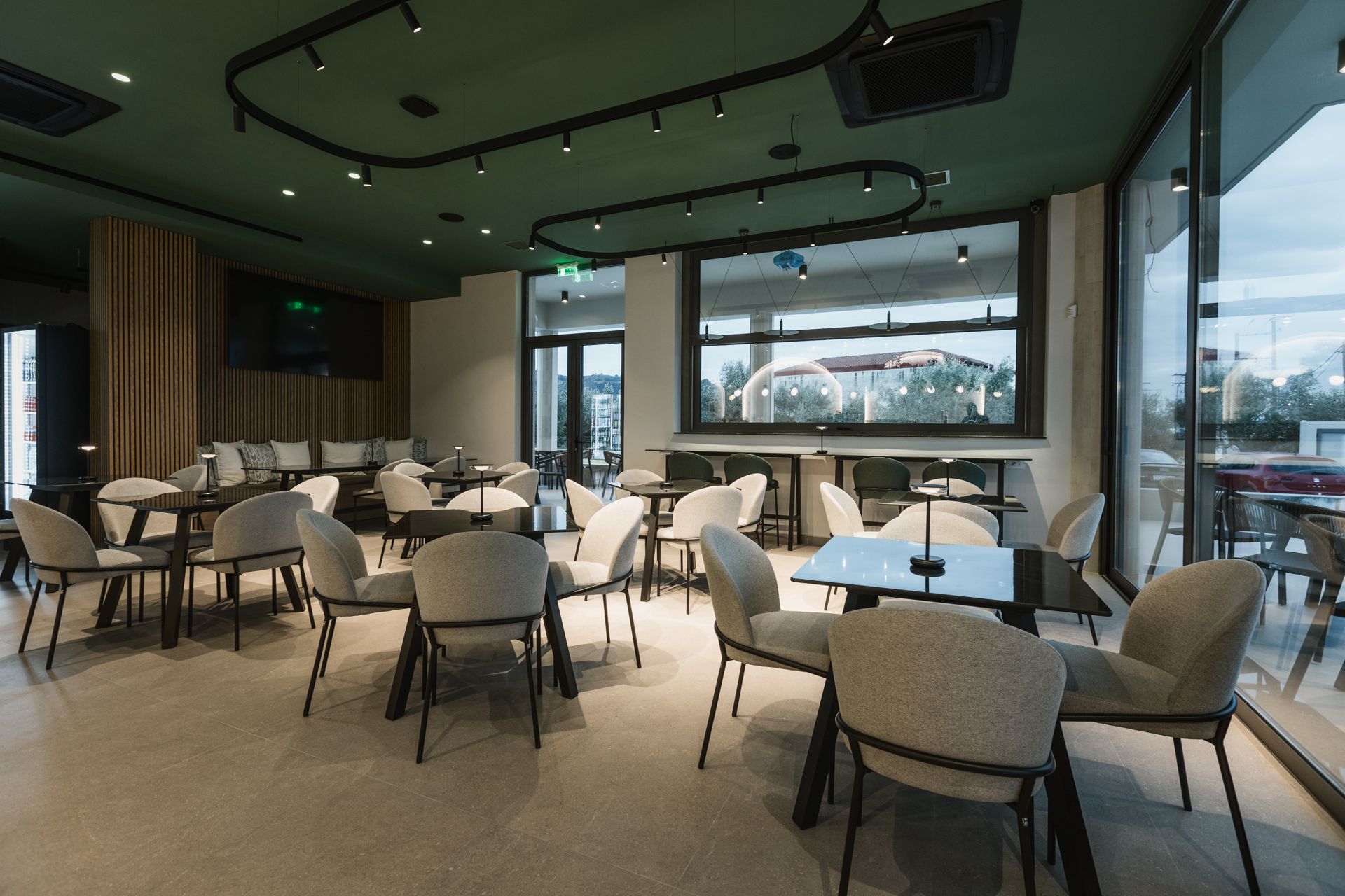 Εσωτερικός χώρος μοντέρνου καφέ με γκρι καθίσματα, ξύλινους τοίχους και πράσινη οροφή.