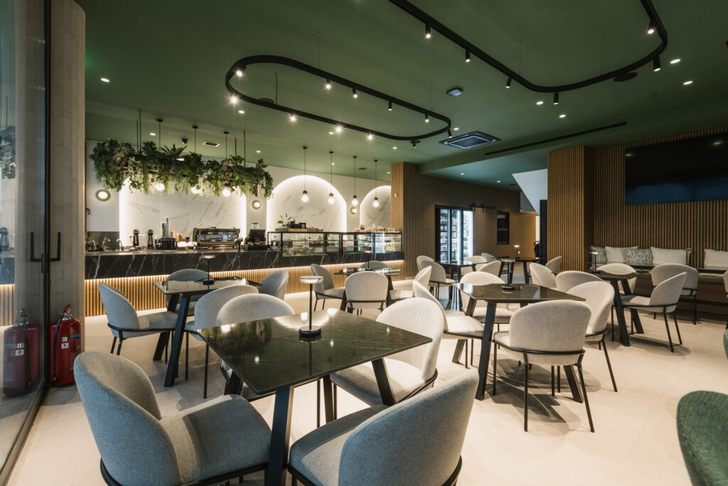 Εσωτερικός χώρος μοντέρνου καφέ με γκρι καθίσματα, ξύλινους τοίχους και πράσινη οροφή.