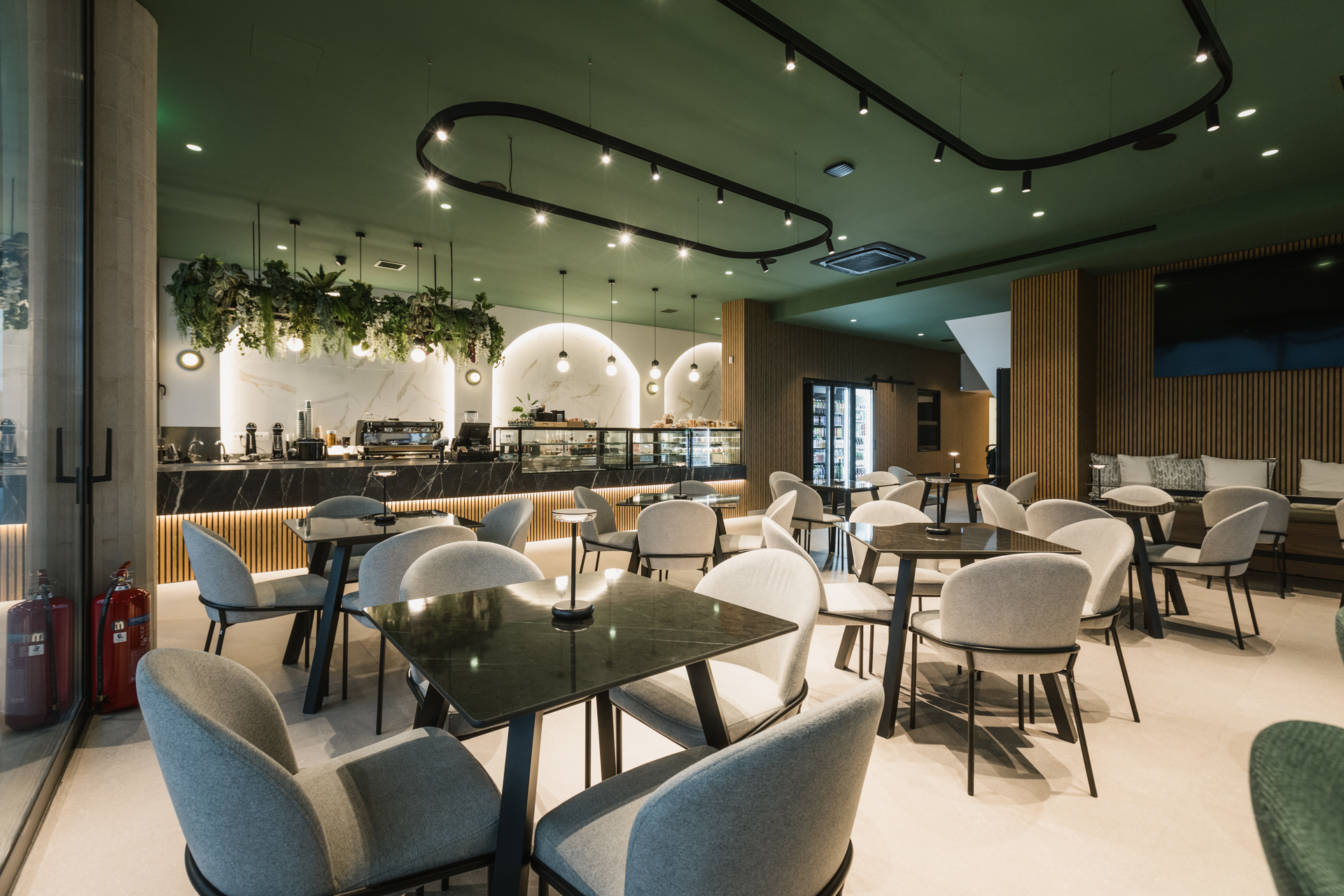 Εσωτερικός χώρος μοντέρνου καφέ με γκρι καθίσματα, ξύλινους τοίχους και πράσινη οροφή.